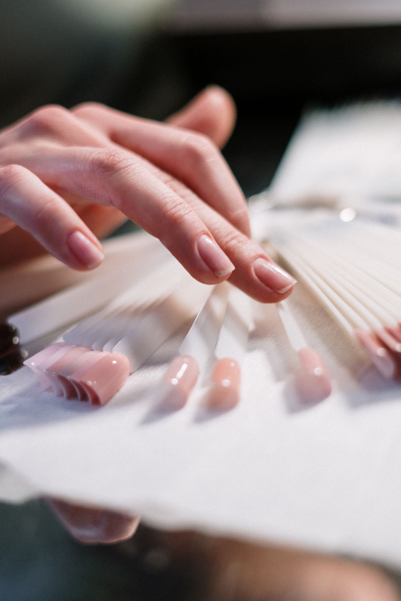 Hand choosing a pink shade from a nail color fan